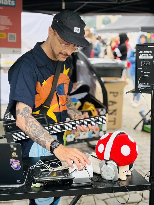 Catbeats performing live outdoors with a mushroom-shaped headphone prop and portable synths on a table