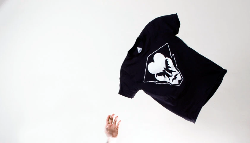 Black t-shirt tossed in the air, printed with a white bat and heart design inside a diamond outline
